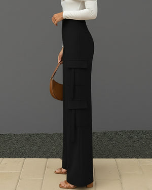 Person wearing black cargo pants and a white top, holding a brown handbag against a gray background.