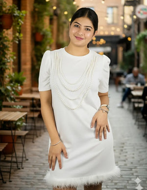 Woman in a white dress with pearl details standing in an outdoor setting.