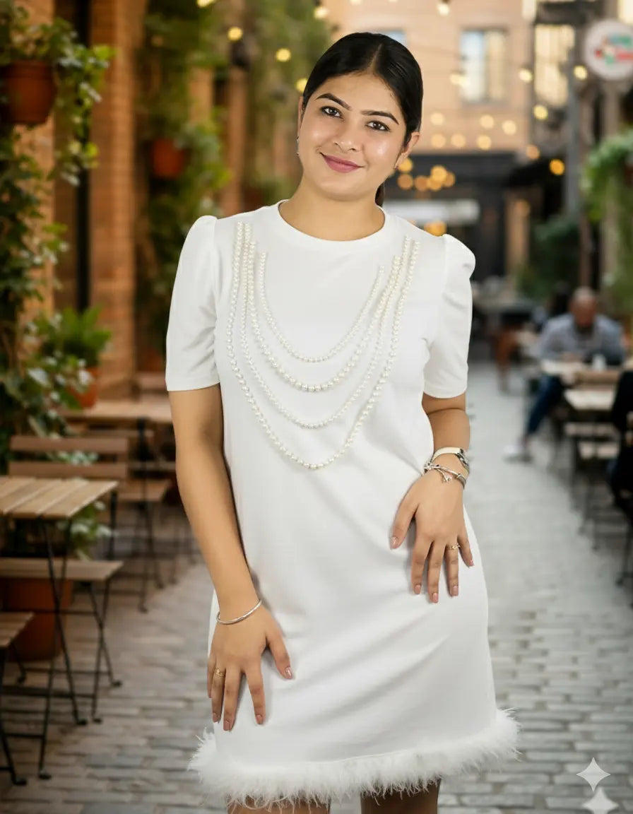 Woman in a white dress with pearl details standing in an outdoor setting.