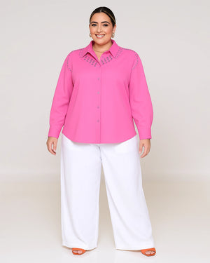 Woman wearing a pink blouse with lace details and white pants on a plain background