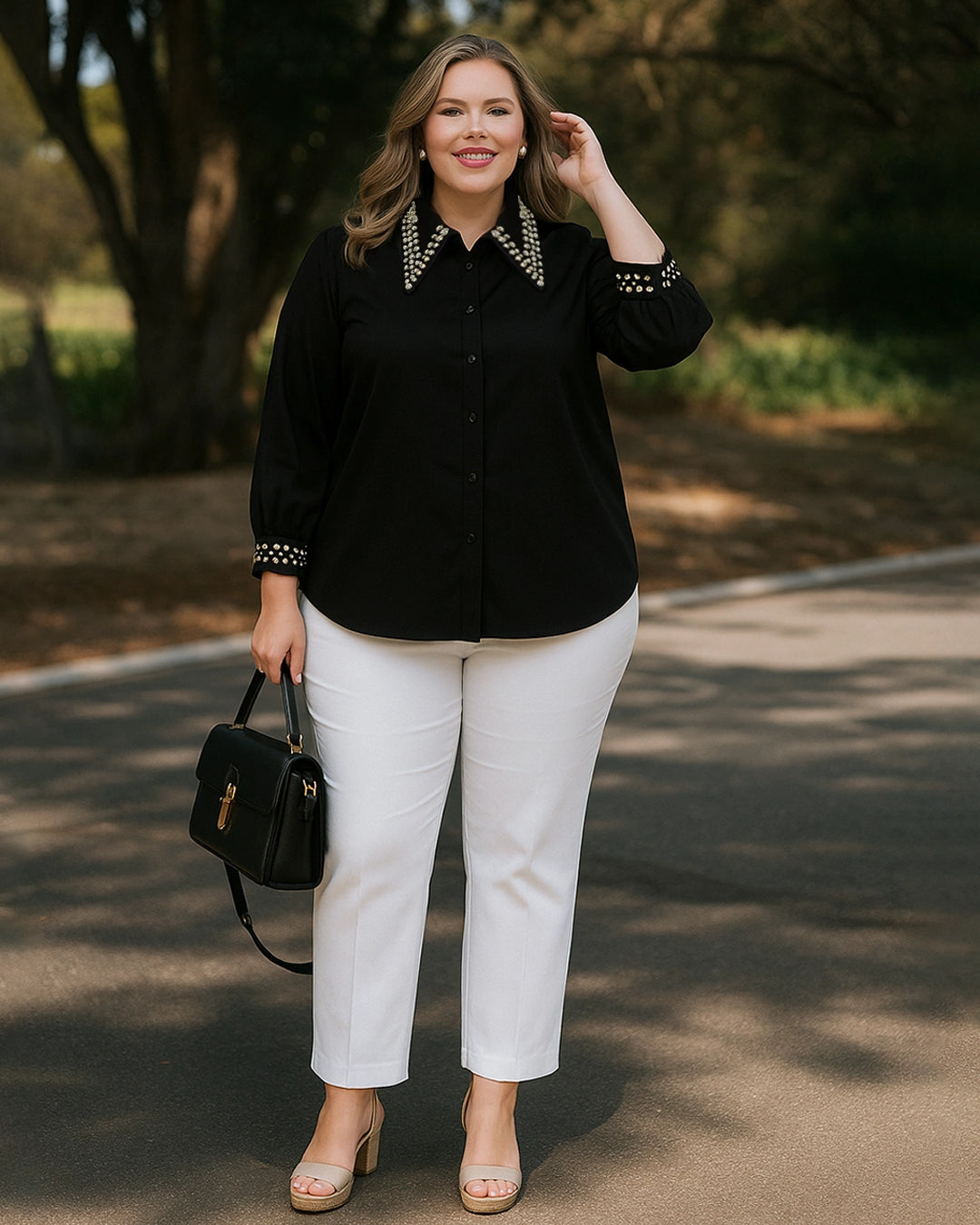 Woman wearing a black blouse with pearl details and white pants, standing outdoors.