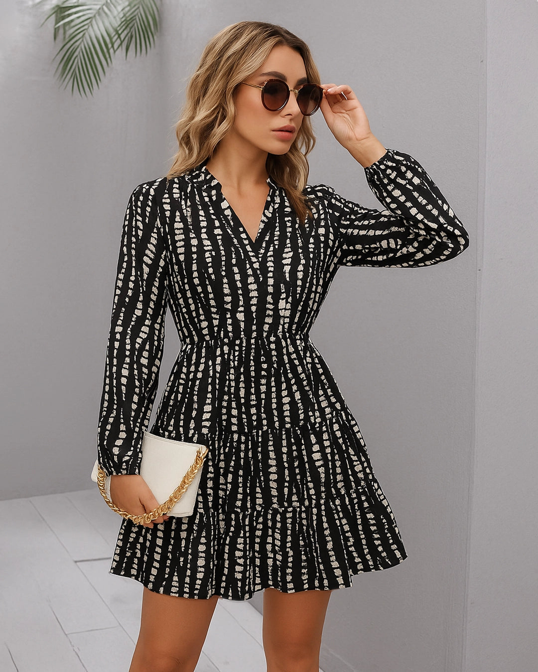 Woman wearing a black and white patterned dress with sunglasses against a gray background