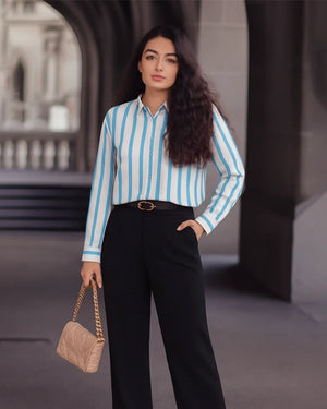 Woman wearing a blue and white striped shirt with black pants, standing in an outdoor setting.