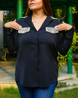 Woman wearing a black blouse with decorative embellishments outdoors.