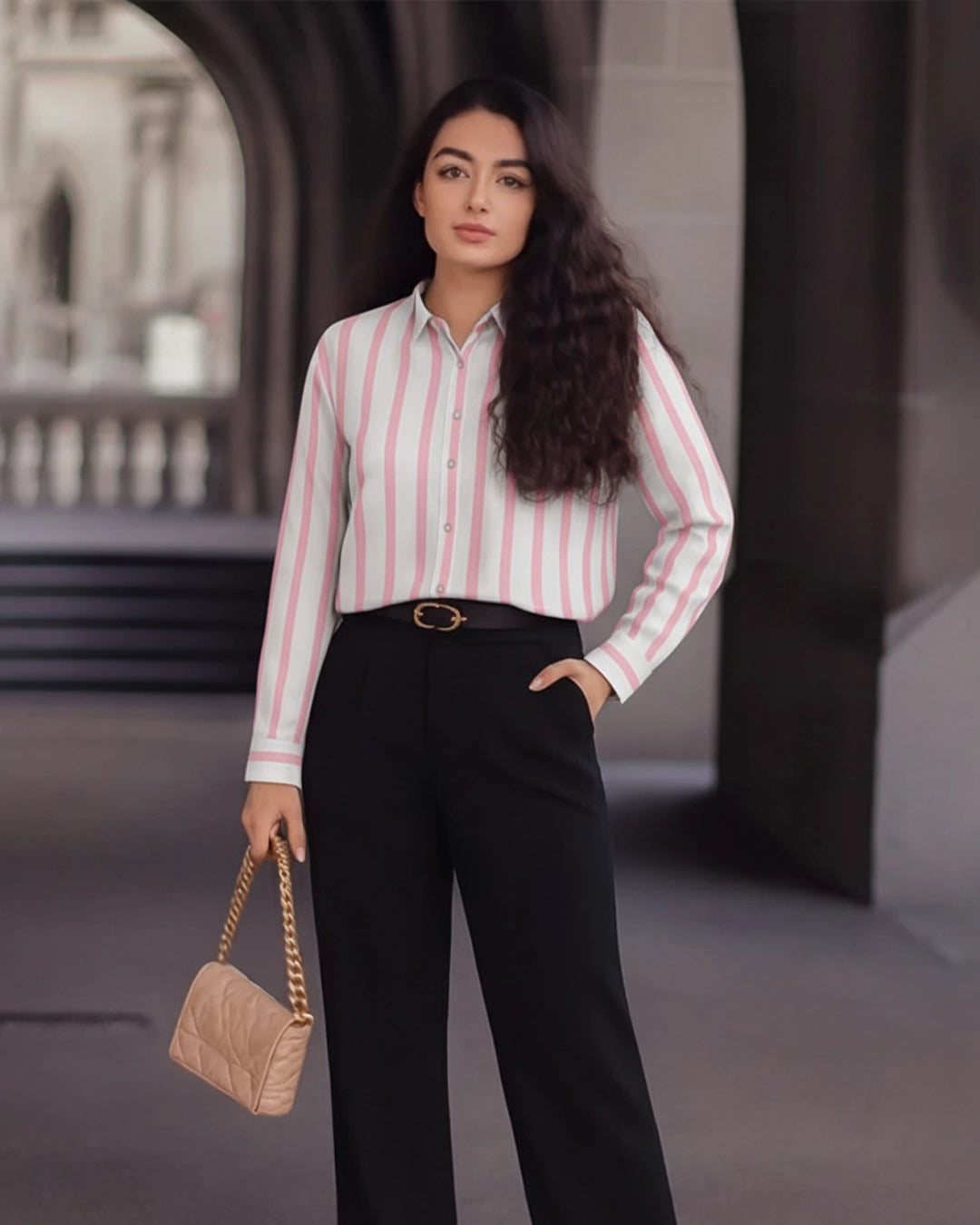 Woman in a striped shirt and black pants holding a beige handbag in an urban setting.