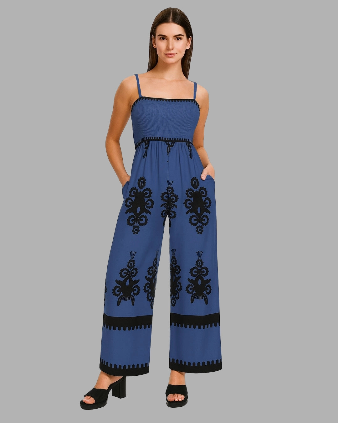 Woman wearing a blue jumpsuit with black embroidery on a gray background