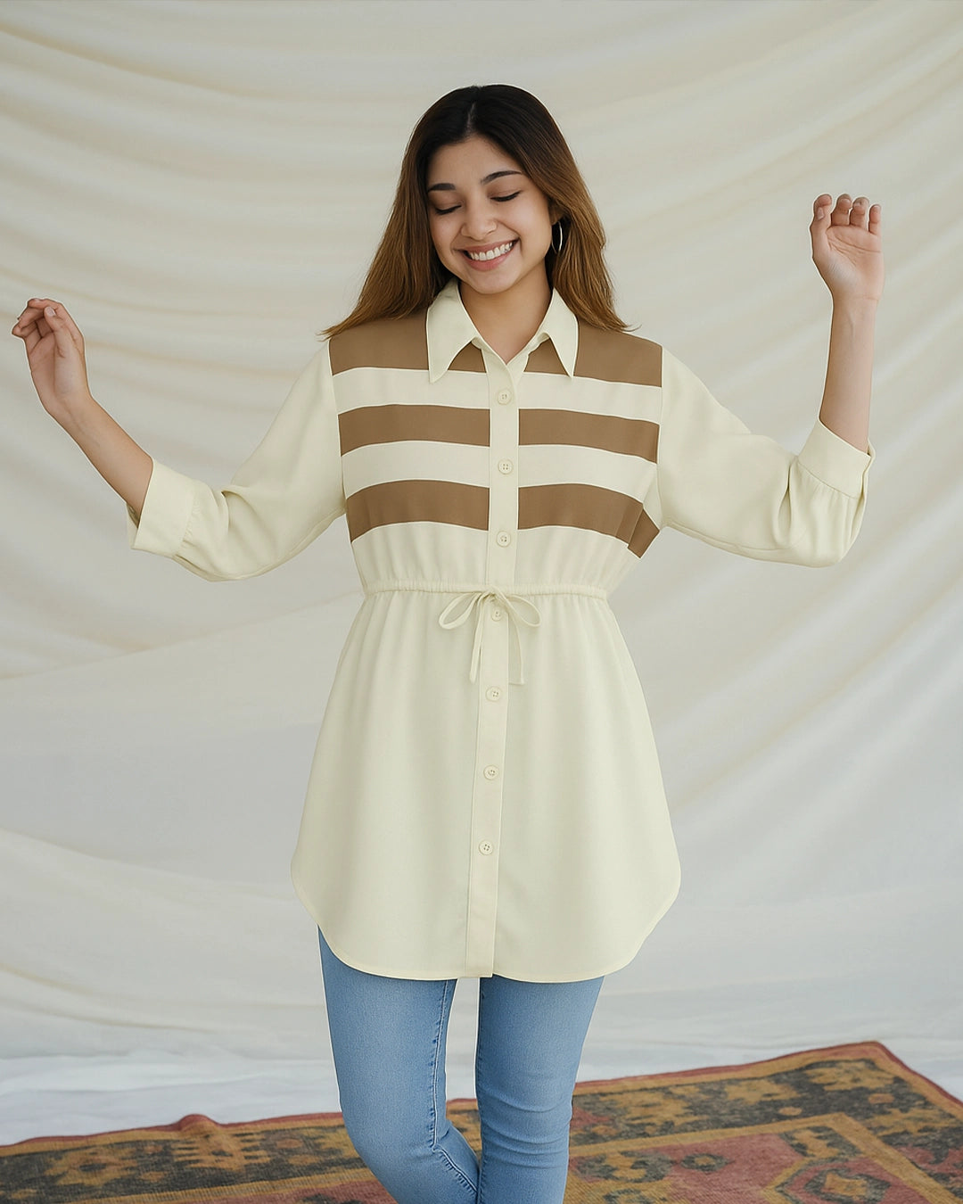 Woman wearing a cream shirt with brown stripes and blue jeans against a plain background