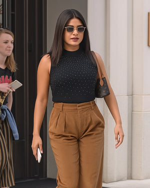 Woman wearing a black sleeveless top and brown pants walking outdoors.