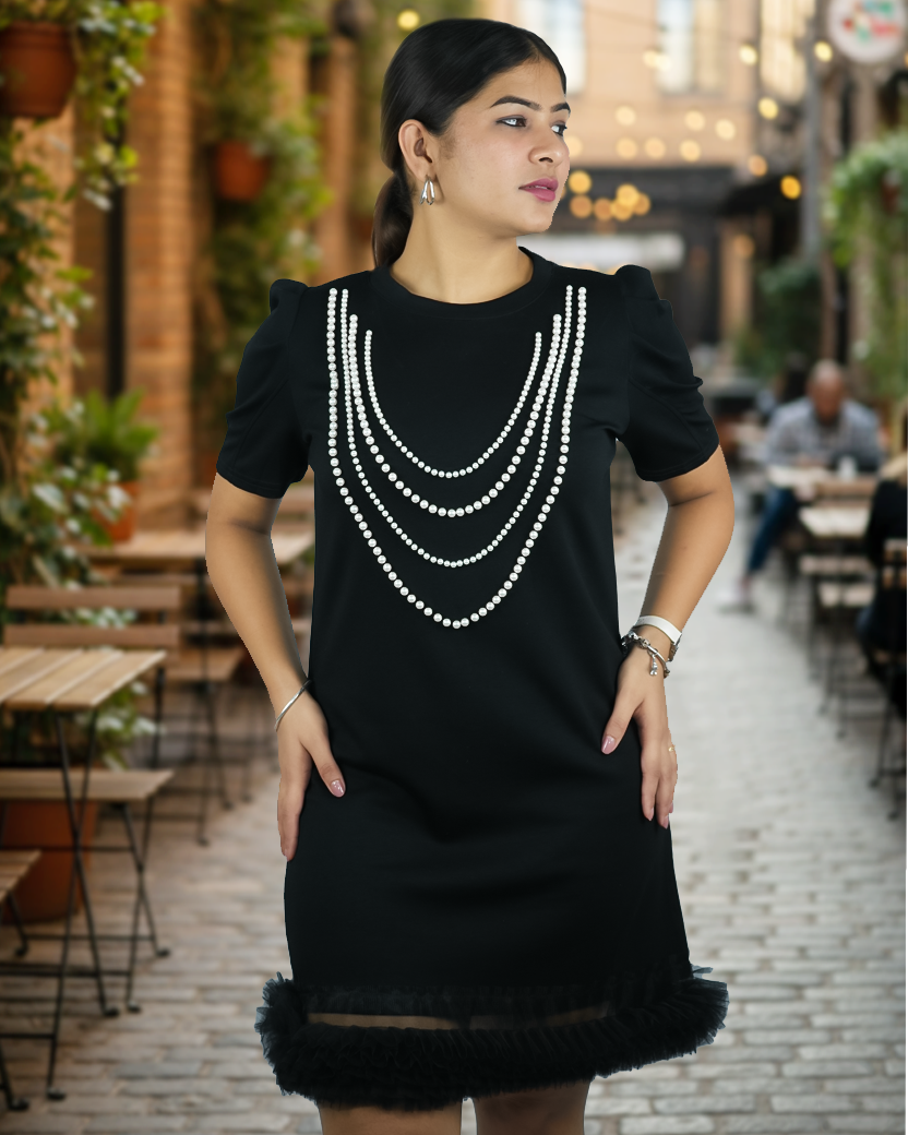 Woman wearing a black dress with white pearl-like embellishments in an outdoor setting.