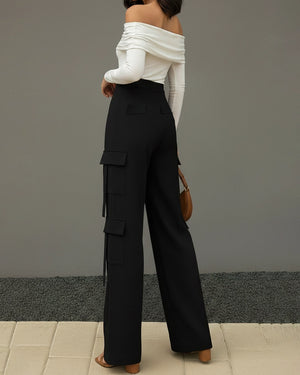 Person wearing black cargo pants and a white off-shoulder top against a gray background