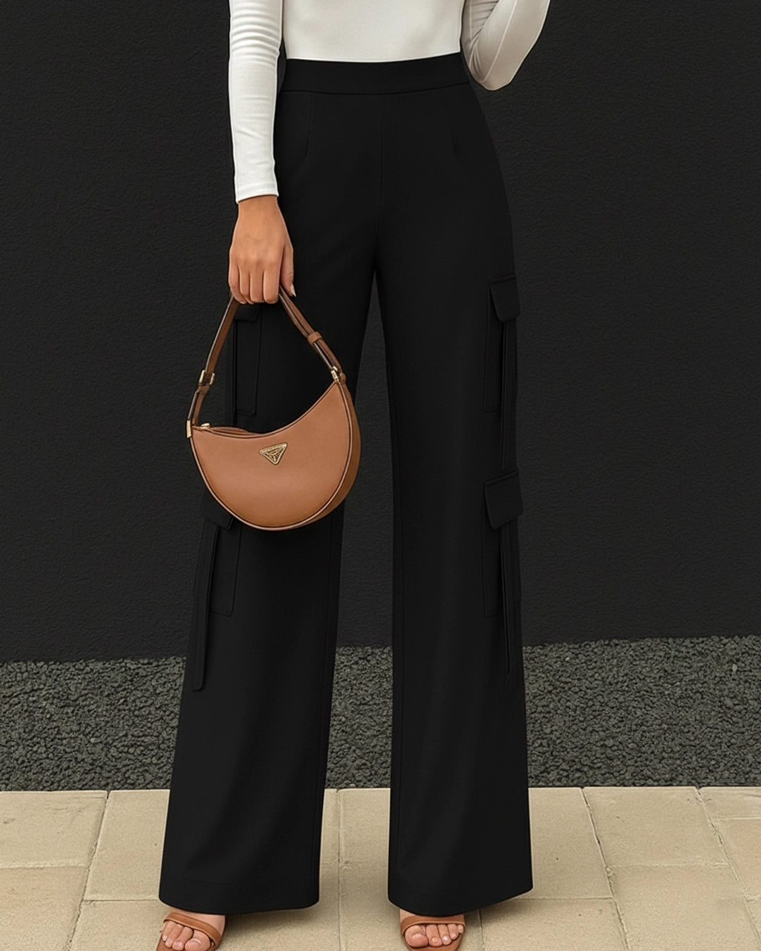 Person wearing black wide-leg pants and holding a brown handbag against a black background