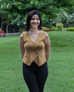 Woman wearing a mustard yellow top and black pants standing in a garden.