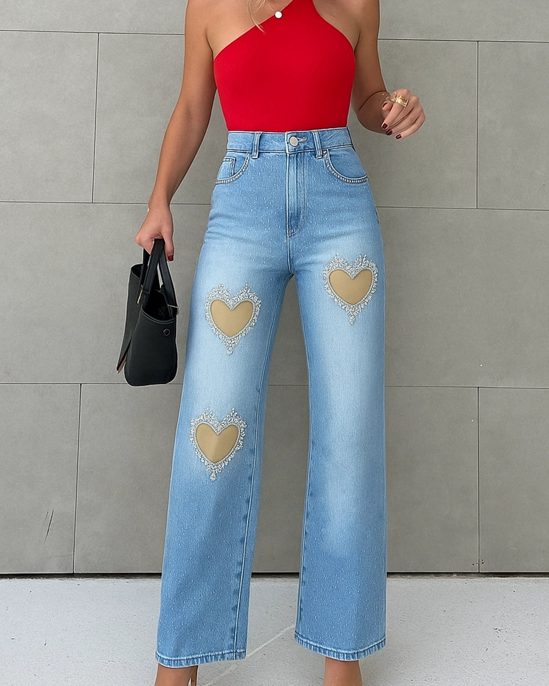 Person wearing red top and blue jeans with heart designs against a gray wall.