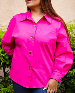 Person wearing a bright pink shirt with buttons against a blurred green and beige background