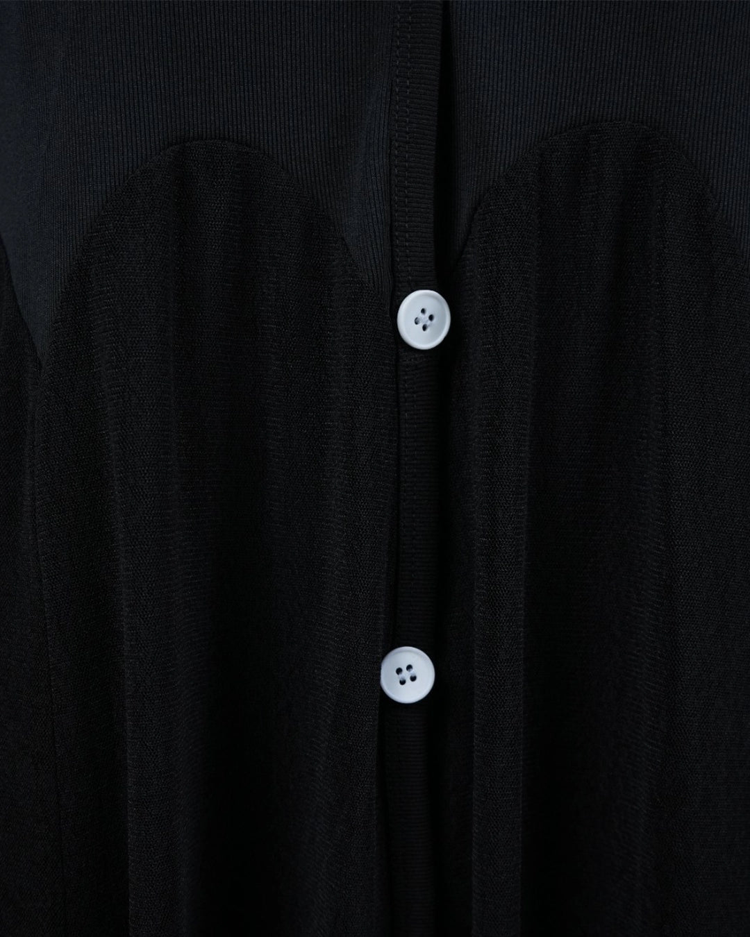 Close-up of a black garment with white buttons on a dark background