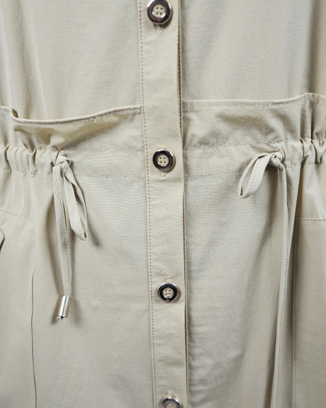 Close-up of a beige jacket with button details and drawstring waist.