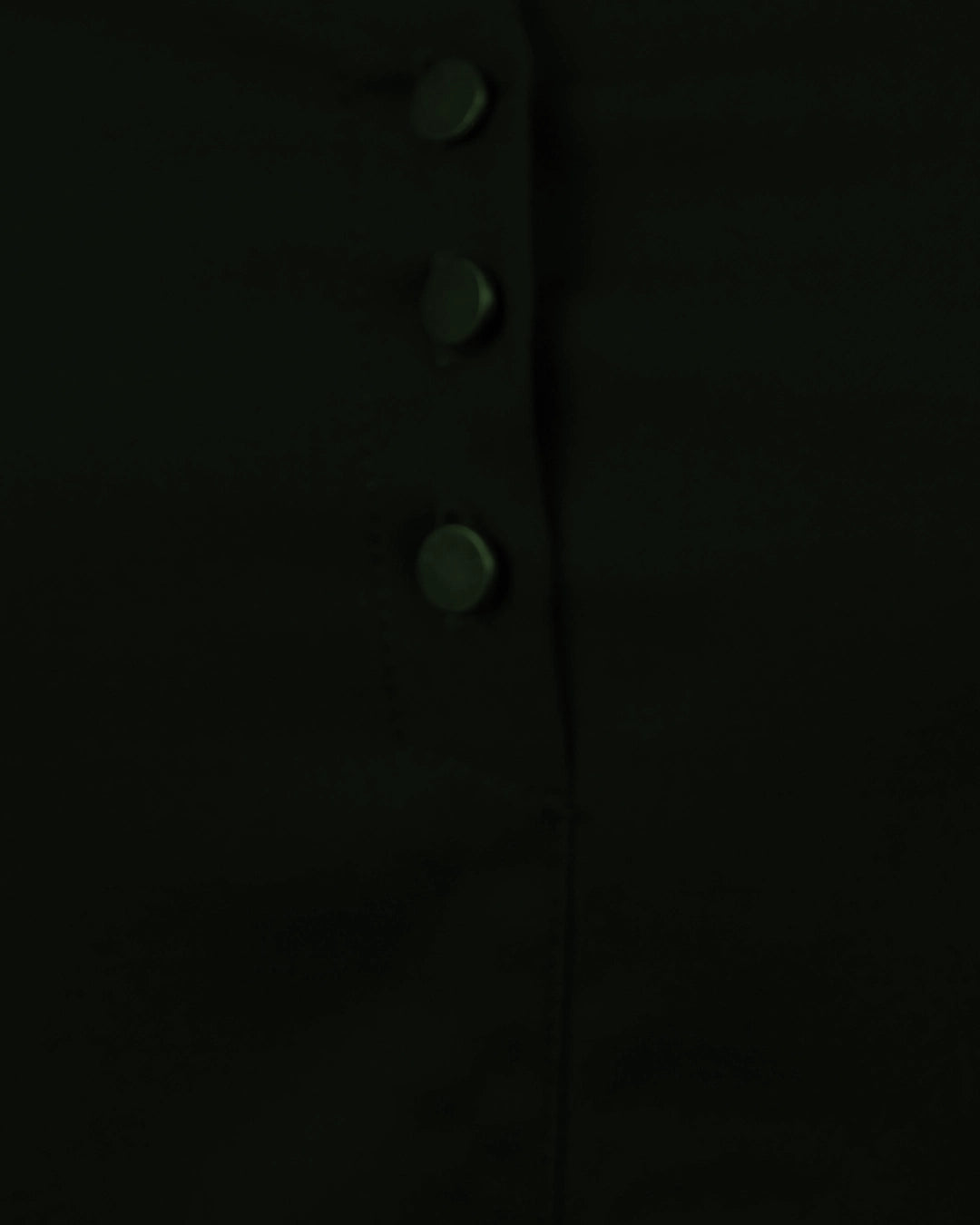 Close-up of a dark coat with button details on a black background