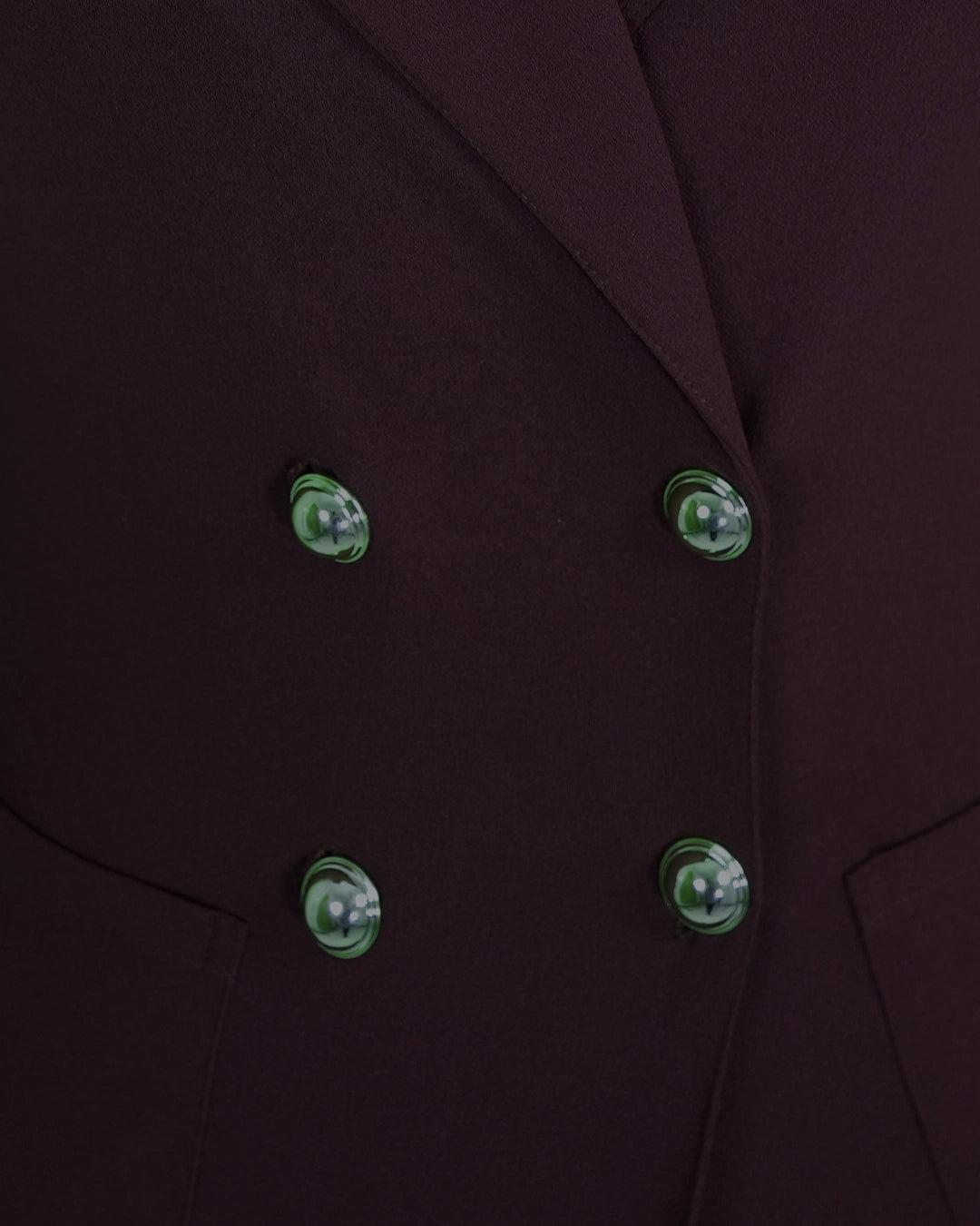 Close-up of a dark coat with green buttons on a matching background