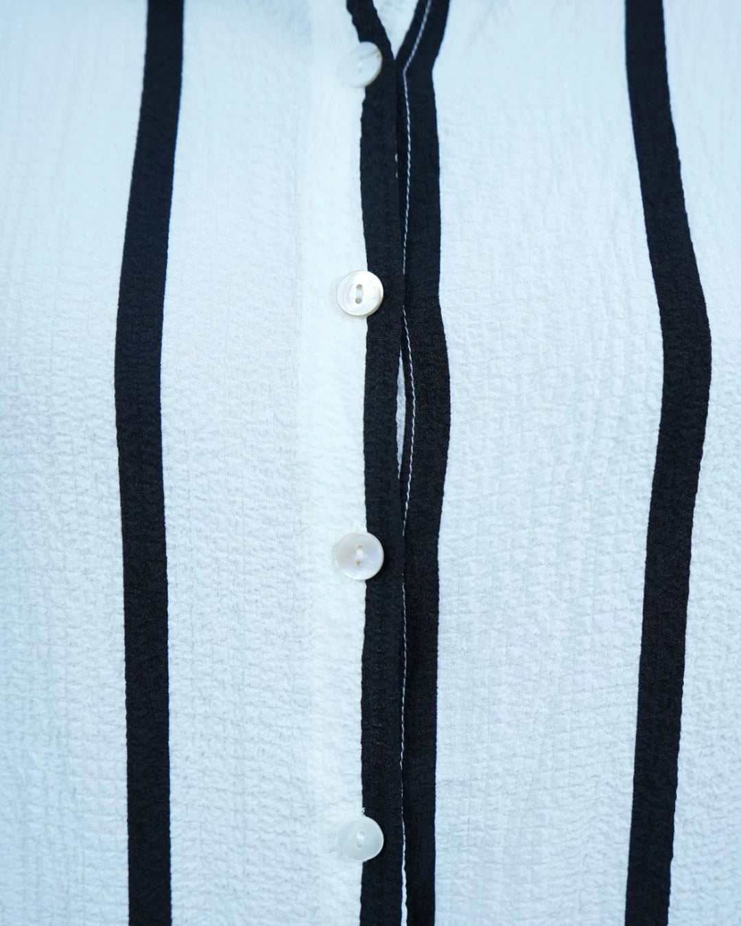 Close-up of a light blue textured fabric with black stripes and white buttons.