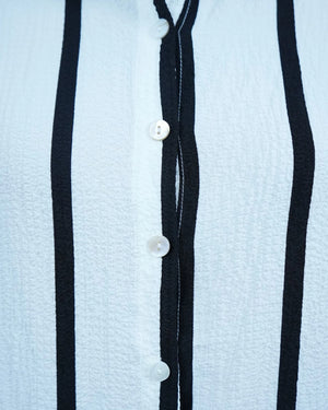 Close-up of a light blue textured fabric with black stripes and white buttons.
