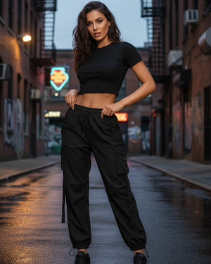 Woman in black crop top and cargo pants standing on a city street at dusk.