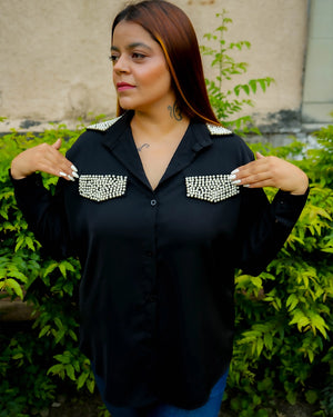 Woman wearing a black shirt with decorative elements, standing outdoors.