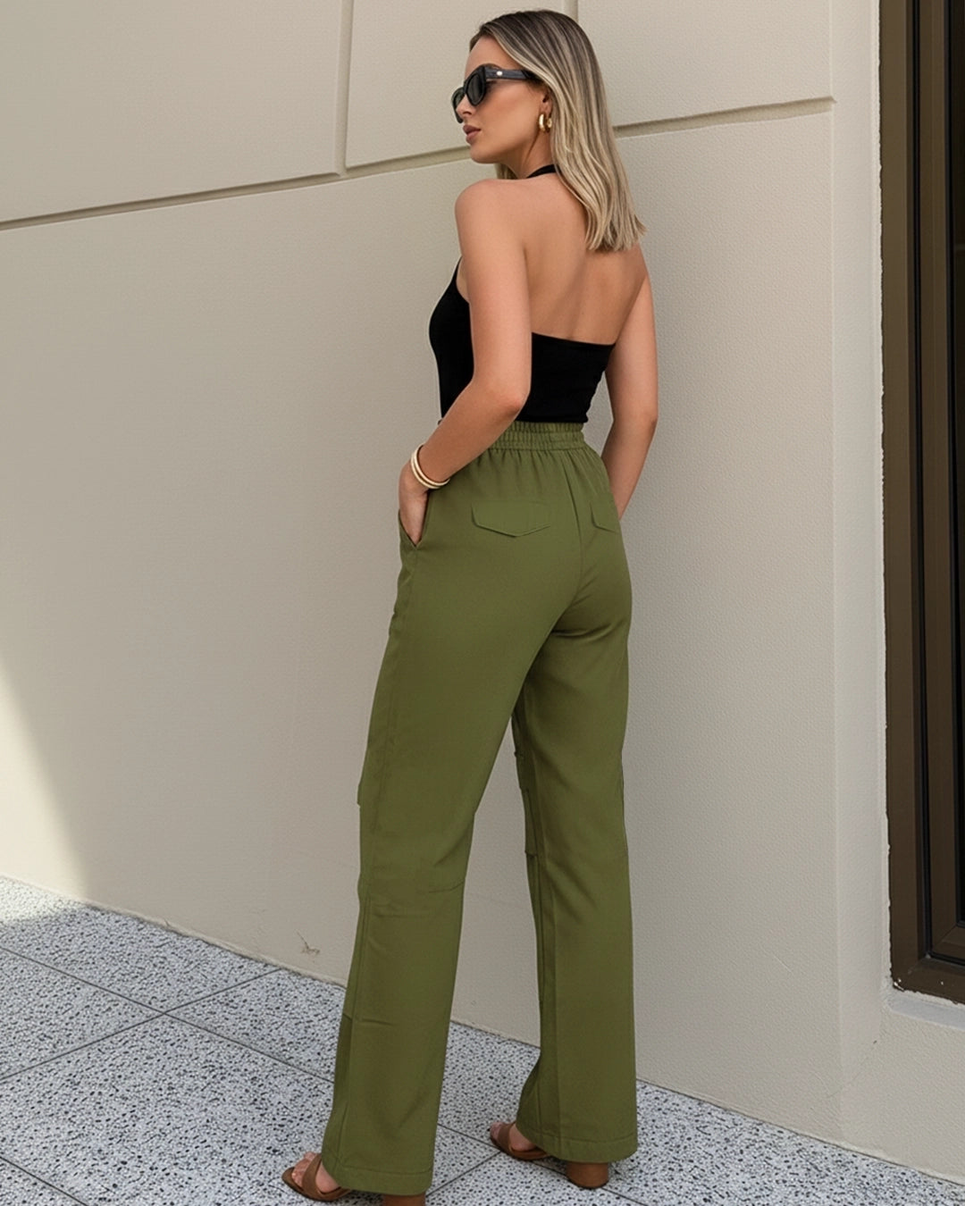 Woman wearing a black strapless top and green high-waisted pants against a beige wall.