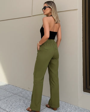 Woman wearing a black strapless top and green high-waisted pants against a beige wall.