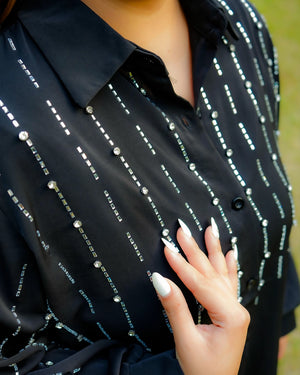 Black shirt with white embellishments worn by a person, with a blurred background