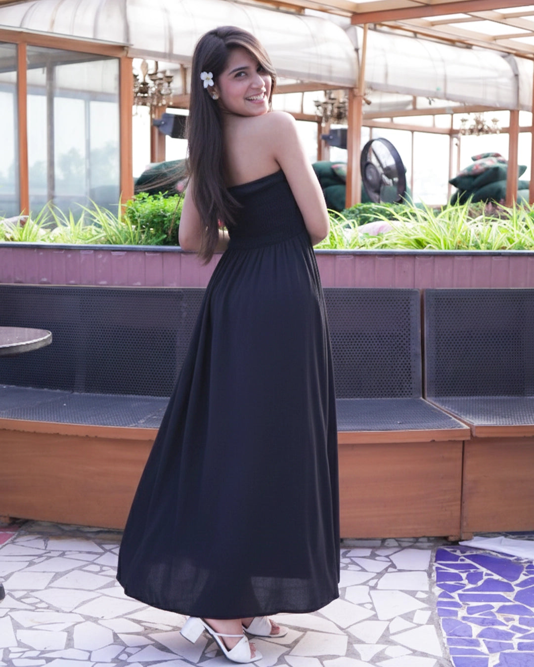 Woman in a black strapless dress standing outdoors with plants and tables in the background