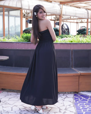 Woman in a black strapless dress standing outdoors with plants and tables in the background