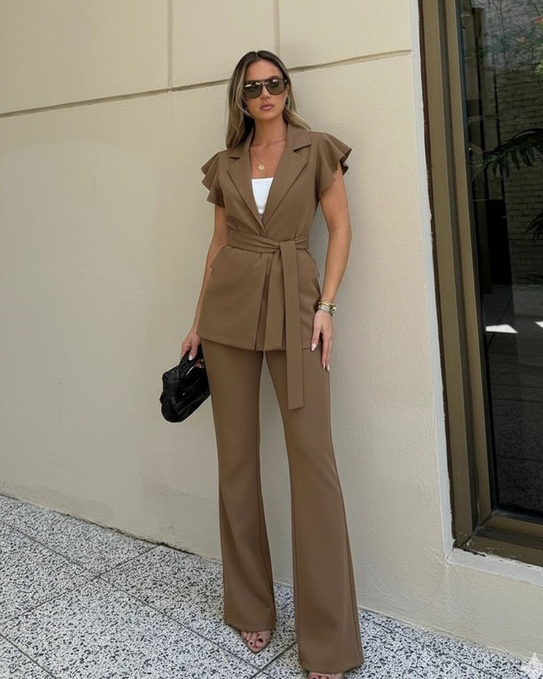 Woman in a brown suit standing against a beige wall.