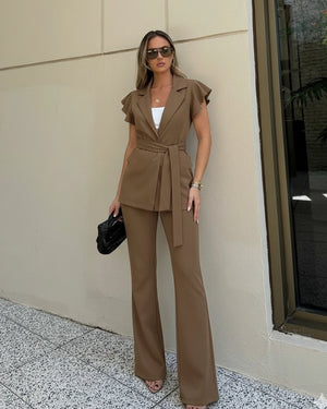 Woman in a brown suit standing against a beige wall.