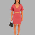 Woman wearing a pink dress holding a black handbag on a gray background