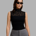 Woman wearing a black lace top and gray pants against a gray background