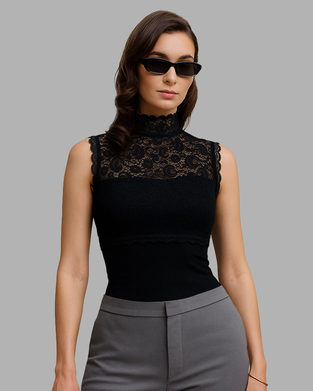Woman wearing a black lace top and gray pants against a gray background