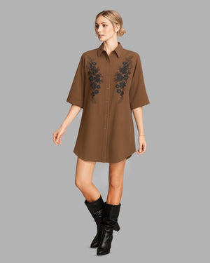 Woman wearing a brown dress with floral embroidery and black boots on a gray background