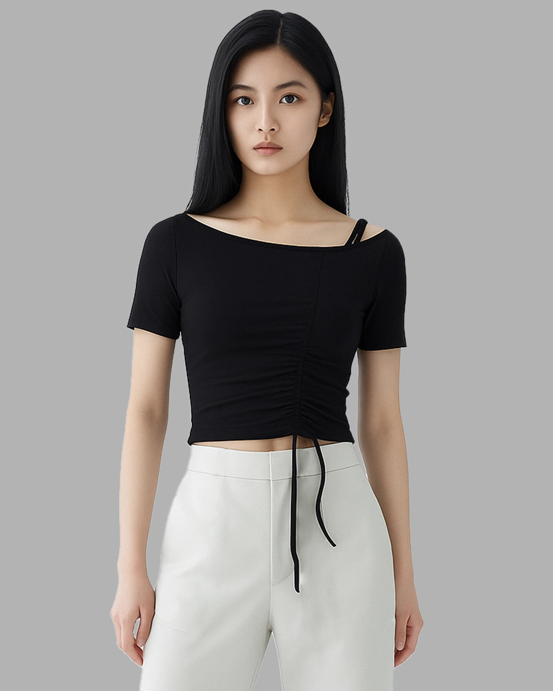 Woman wearing a black ruched top and white pants against a gray background