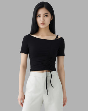 Woman wearing a black ruched top and white pants against a gray background
