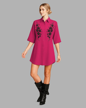 Woman wearing a pink dress with black floral embroidery on a gray background