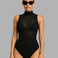 Woman wearing a black polka dot swimsuit against a gray background