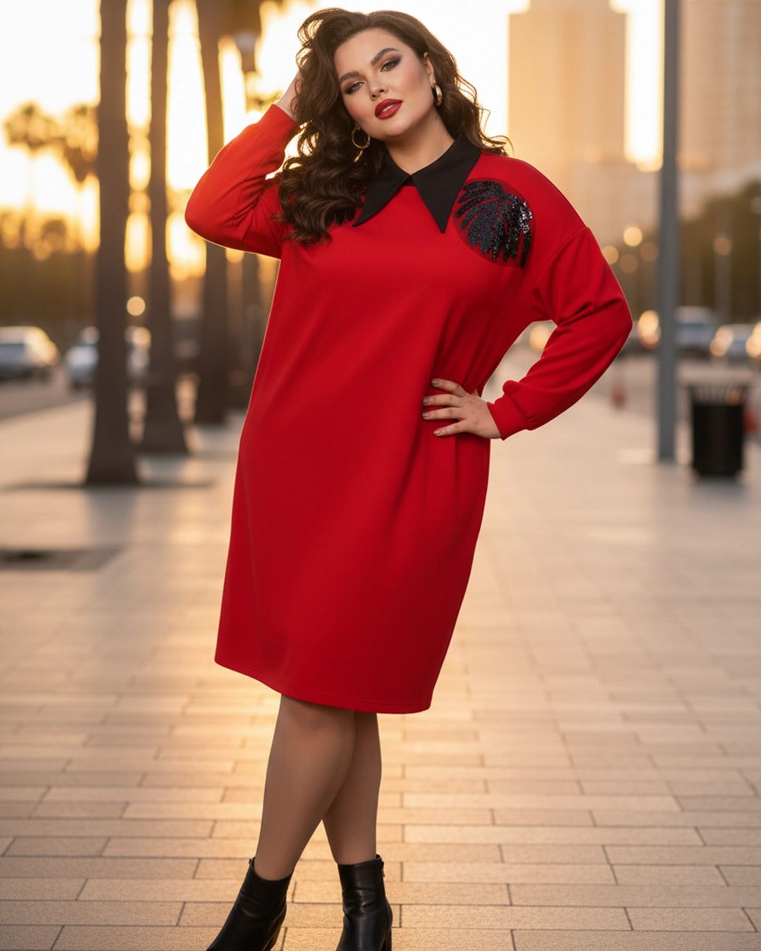 Woman wearing a red dress with black details on a city street at sunset.