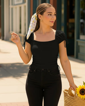 Woman in black outfit with a colorful headscarf and sunflower, standing outdoors.
