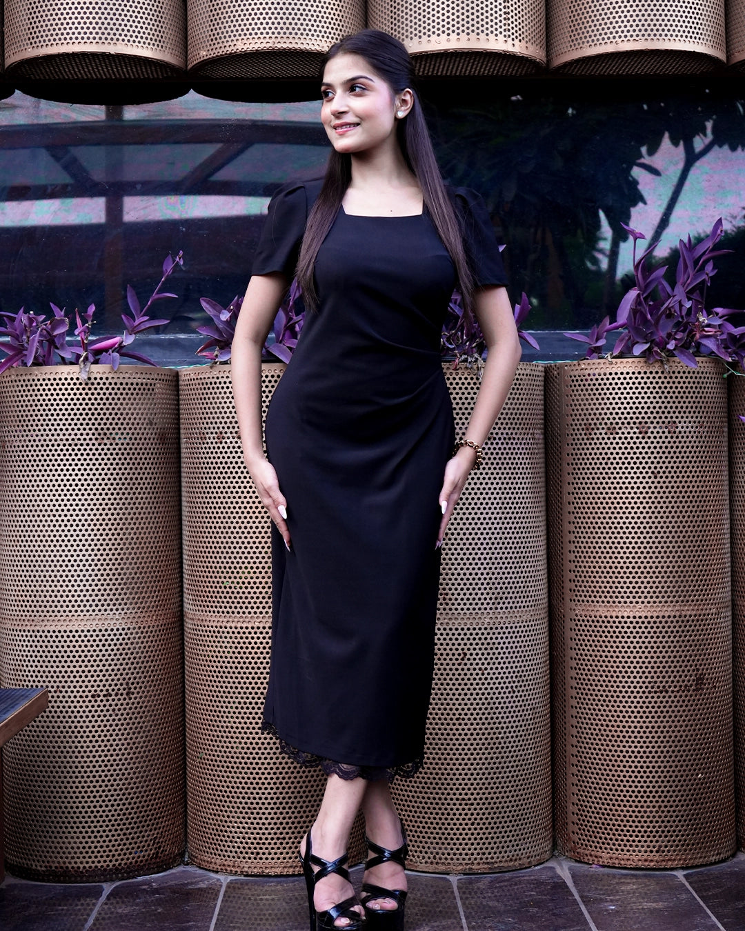 Woman in a black dress standing in front of decorative planters with a dark background