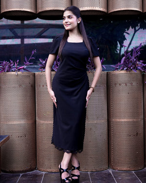 Woman in a black dress standing in front of decorative planters with a dark background