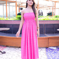 Woman in a pink dress standing in an outdoor setting with plants and tables.