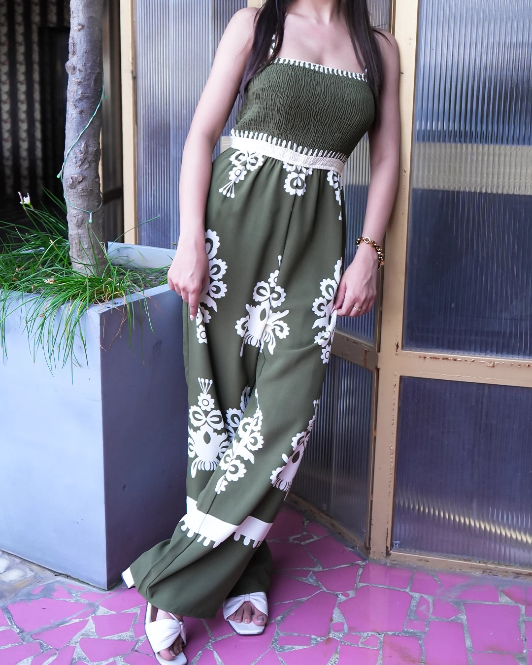 Woman wearing a green dress with white floral patterns standing against a textured wall.