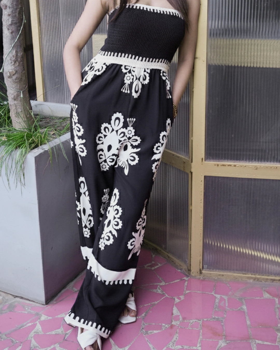 Person wearing a black outfit with white floral patterns standing on a pink tiled floor.