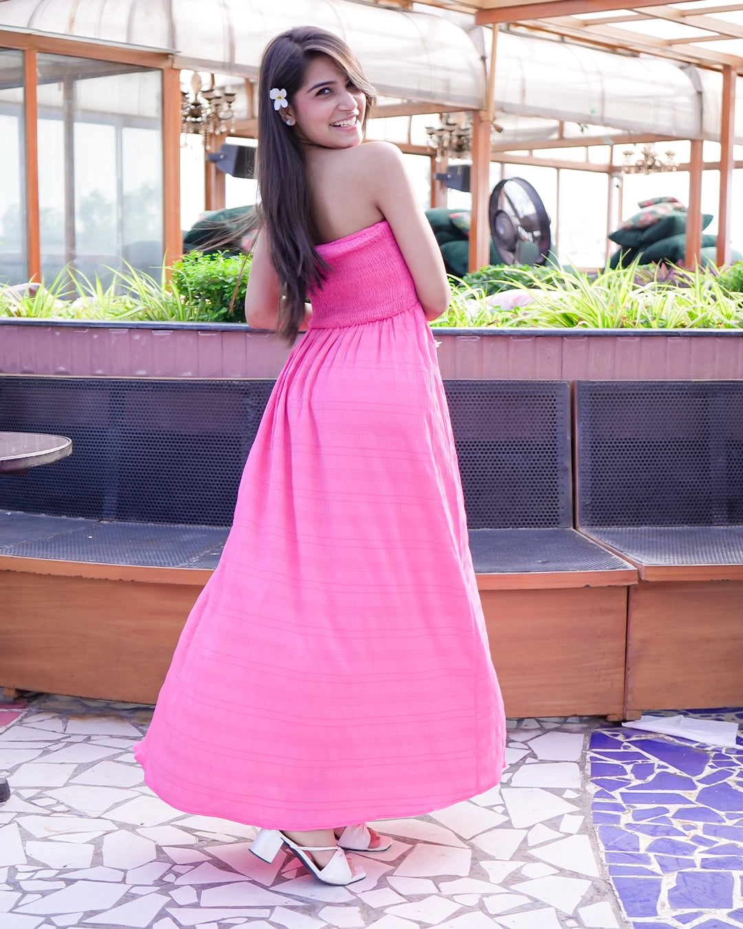 Woman in a pink dress standing outdoors with greenery in the background