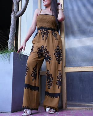 Woman wearing a mustard yellow jumpsuit with black patterns against a textured wall.